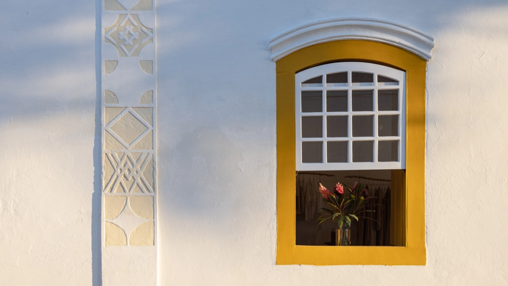 Moldura de janela com toques amarelos intensos contra o calcário branco. Joana França